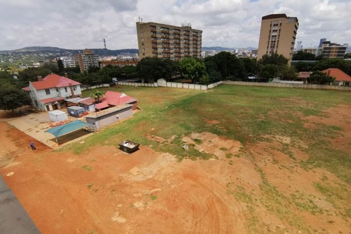 Aerial view of a large vacant residential plot featuring open grass areas, perimeter walling, and existing structures on the adjacent property.