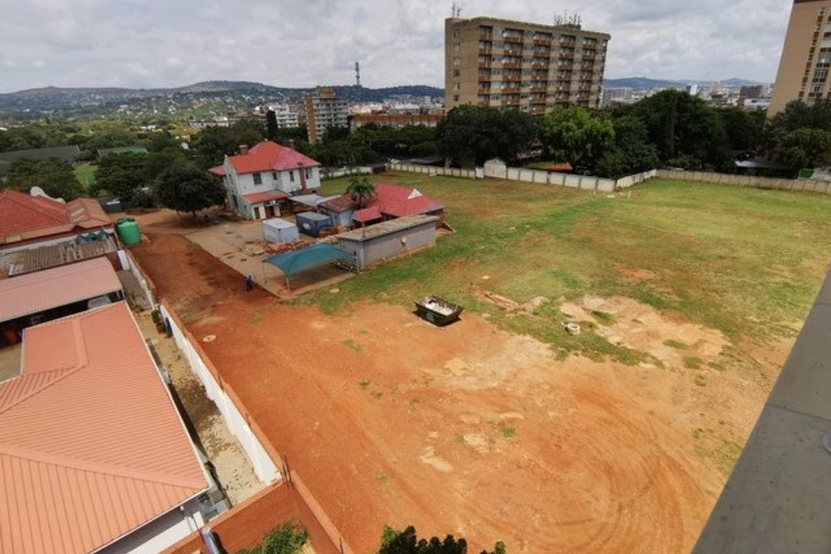 An elevated aerial view of a large vacant residential plot featuring open land, perimeter fencing, and adjacent existing structures.