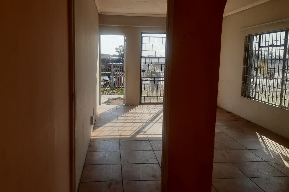 An empty living area featuring tiled flooring, security gates, and burglar bars on the windows, offering a blank canvas for potential renovation.