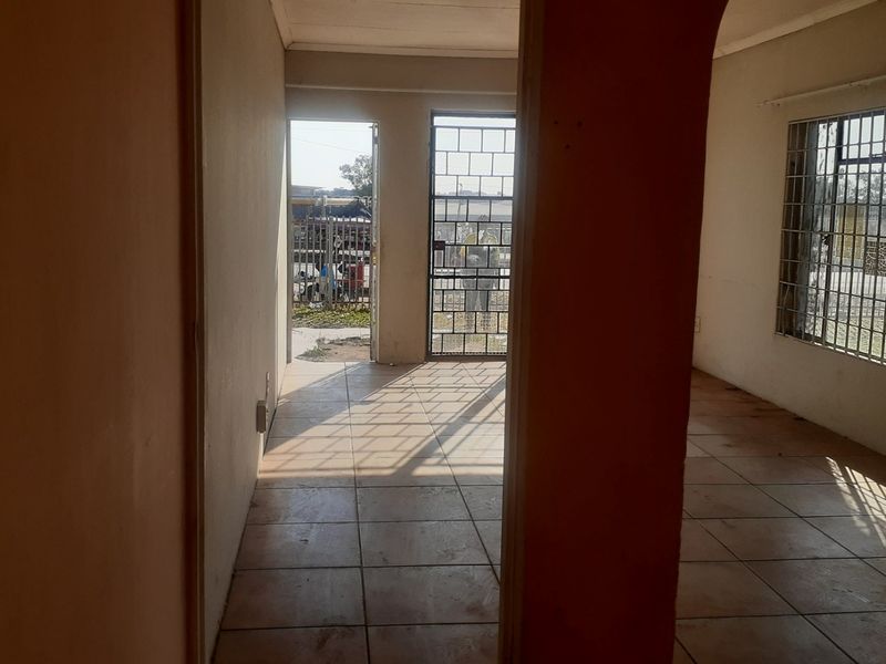An empty living area featuring tiled flooring, security gates, and burglar bars on the windows, offering a blank canvas for potential renovation.