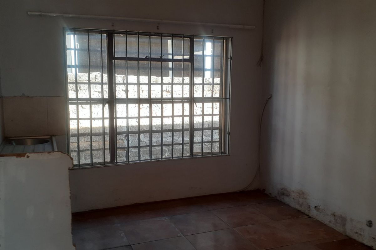 A basic, empty kitchen area featuring tiled flooring, a built-in sink, and security bars on the window, requiring cosmetic updates and repairs.