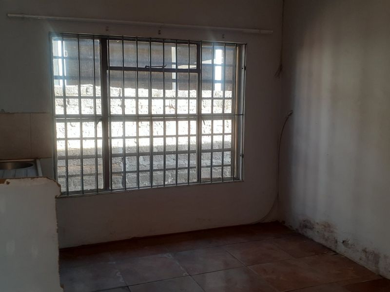 A basic, empty kitchen area featuring tiled flooring, a built-in sink, and security bars on the window, requiring cosmetic updates and repairs.