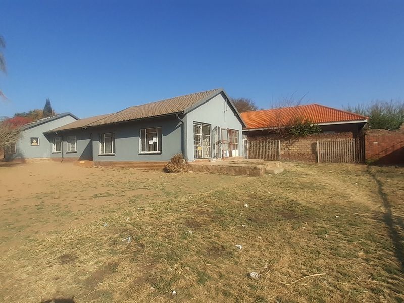 Rear view of a detached house featuring a tiled roof, security bars on windows, and a large, unlandscaped yard area.