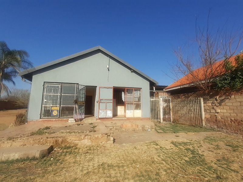 Rear view of a detached house featuring a concrete patio area, security gates, and a brick boundary wall in need of maintenance.