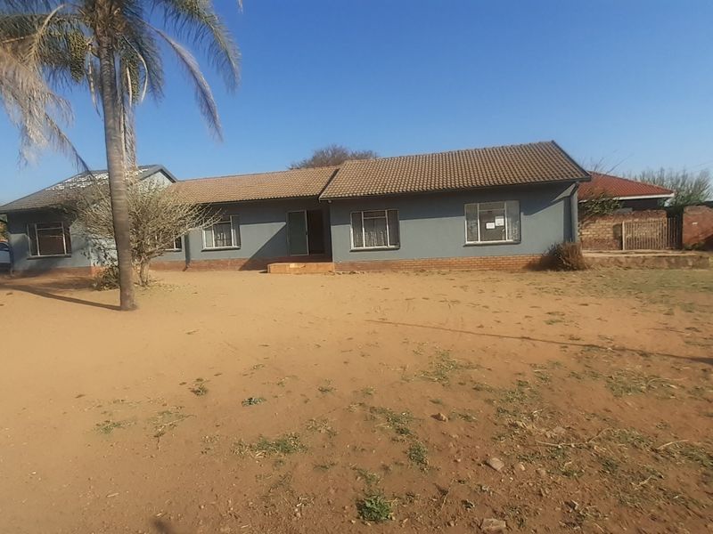Front view of a single-story residential house featuring a tiled roof, brick base, and large windows, set on a spacious, unlandscaped plot.