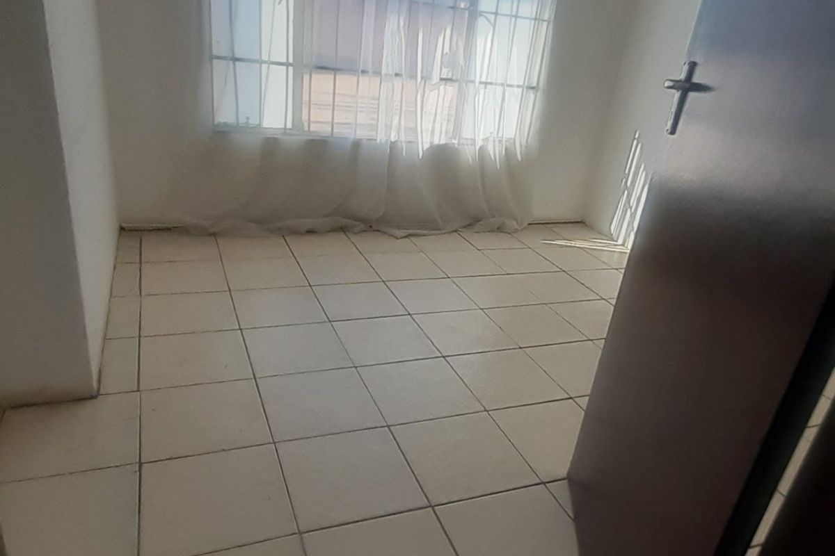 An empty bedroom featuring tiled flooring and a large steel-framed window, providing a blank canvas for potential interior design updates.