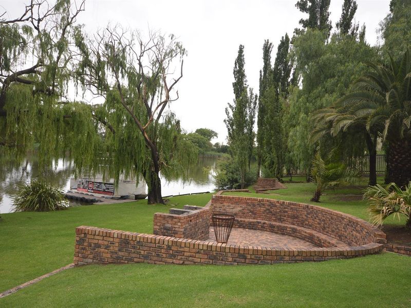 A well-maintained garden area featuring a curved brick seating wall, built-in braai, and paved patio overlooking the water.