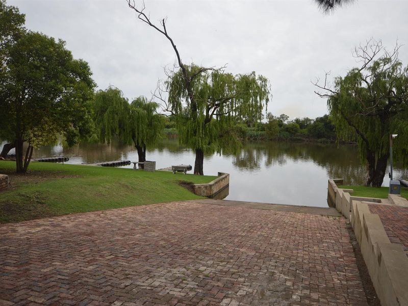 A scenic view of the riverfront featuring a brick-paved boat ramp, landscaped lawn, and mature trees providing direct water access.
