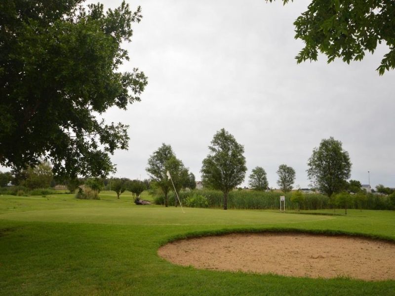 A scenic view of a well-maintained golf course featuring a sand bunker and lush green fairways.