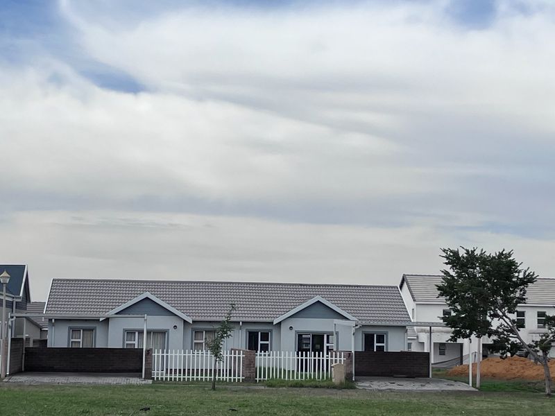 Front elevation of a modern townhouse featuring a tiled roof, paved driveway, carport, and secure white picket fencing.