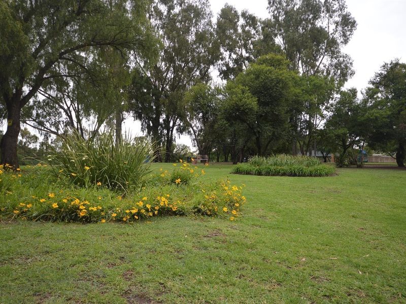 A well-maintained communal garden area featuring established trees, manicured lawn, and landscaped flower beds.