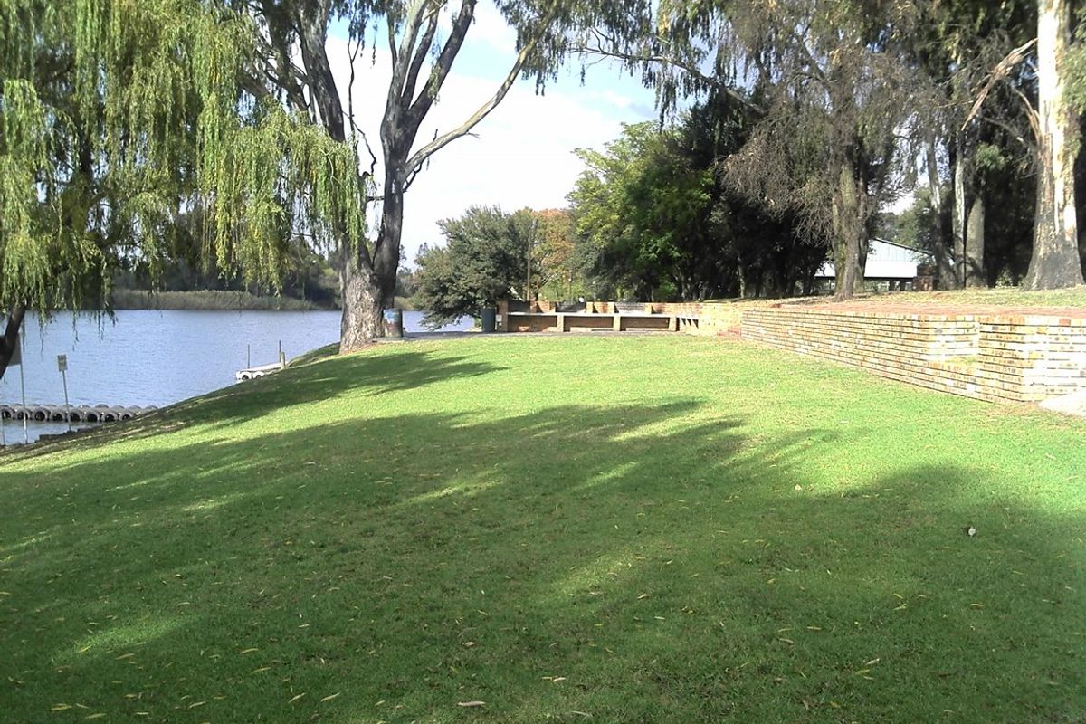 A spacious, well-maintained garden area featuring a brick retaining wall, mature trees, and direct access to the waterfront.