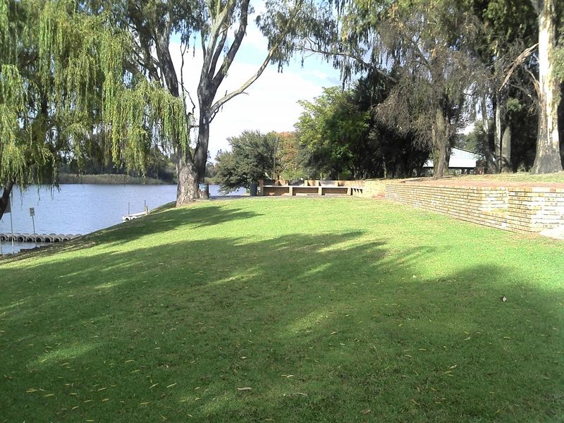 A spacious, well-maintained garden area featuring a brick retaining wall, mature trees, and direct access to the waterfront.