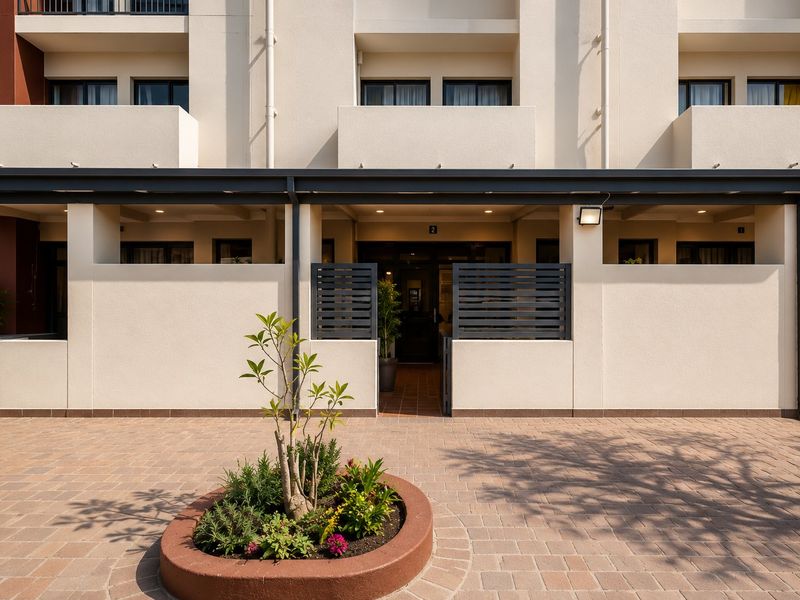 Modern apartment building entrance featuring a paved courtyard, brick planter, and covered walkway with integrated privacy screens and exterior lighting.