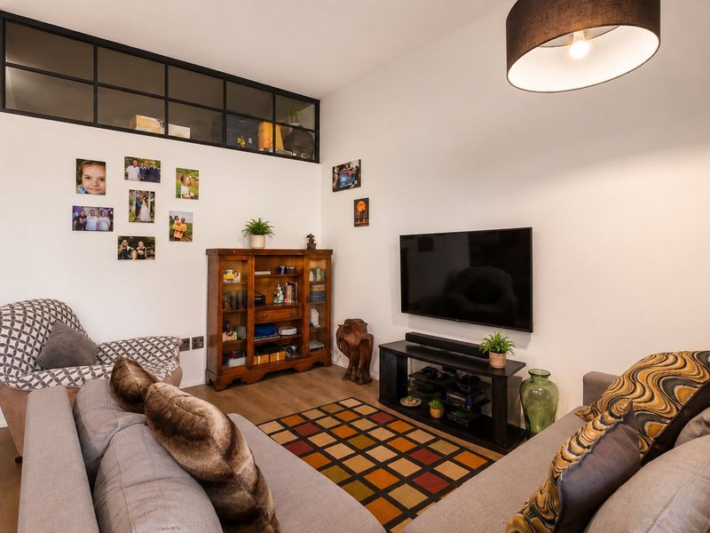 A cozy living room featuring laminate flooring, a high-level transom window, and a central pendant light fixture.