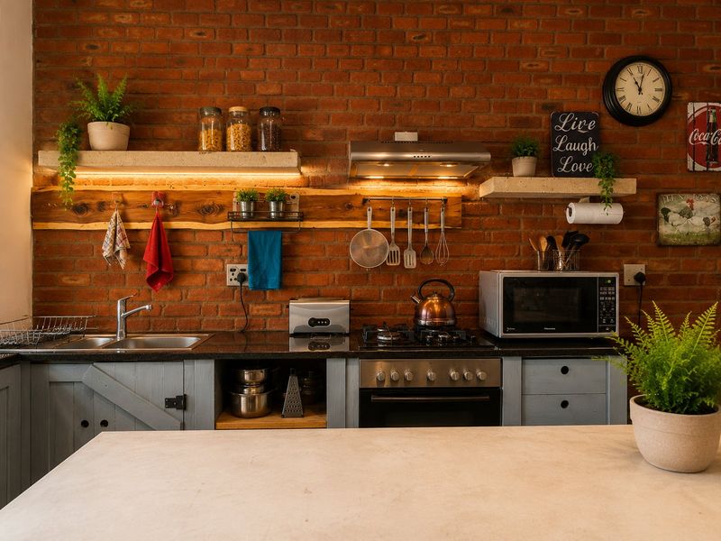 A charming kitchen featuring an exposed brick wall, stone countertops, built-in oven, gas cooktop, and stylish floating shelves with integrated lighting.