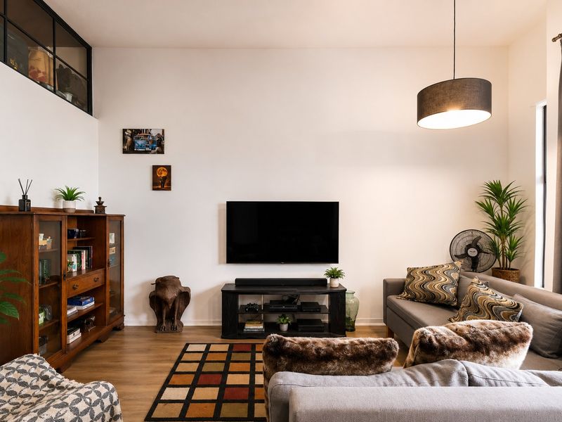 A well-maintained living room featuring high ceilings, laminate flooring, and a clerestory window, creating a bright and spacious atmosphere.
