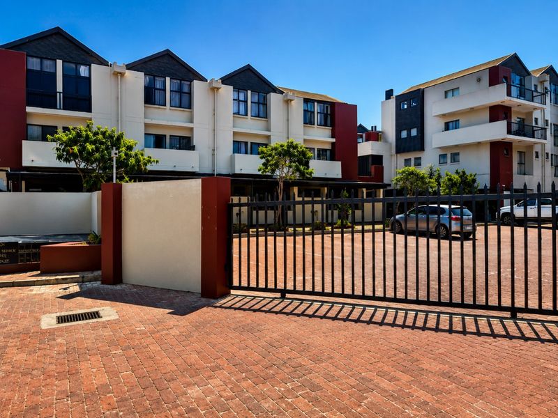 Front view of a modern apartment complex featuring a secure gated entrance, brick paved driveway, and multi-level residential units with balconies.