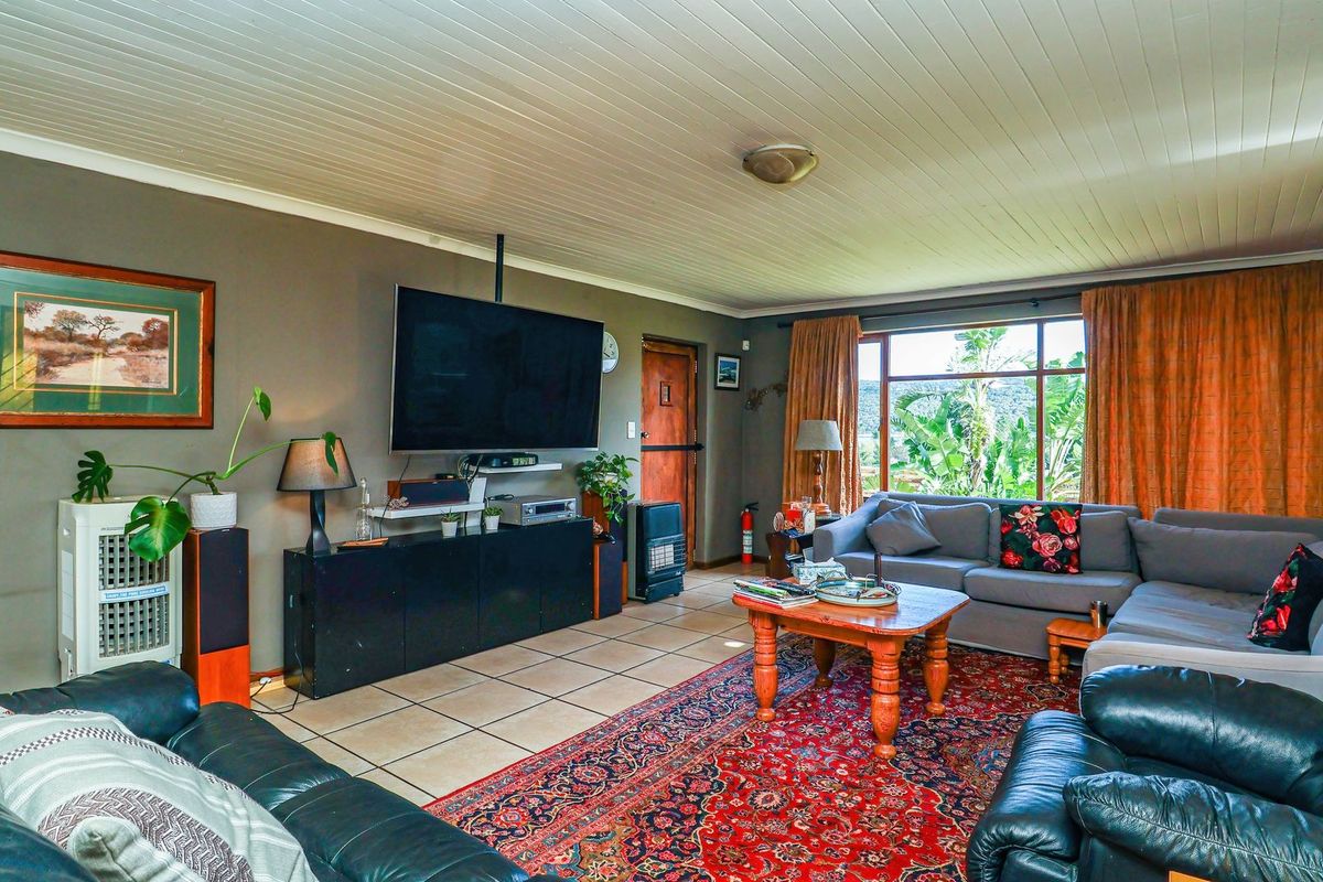 A spacious living room featuring tiled flooring, a tongue and groove ceiling, and large windows providing natural light and garden views.