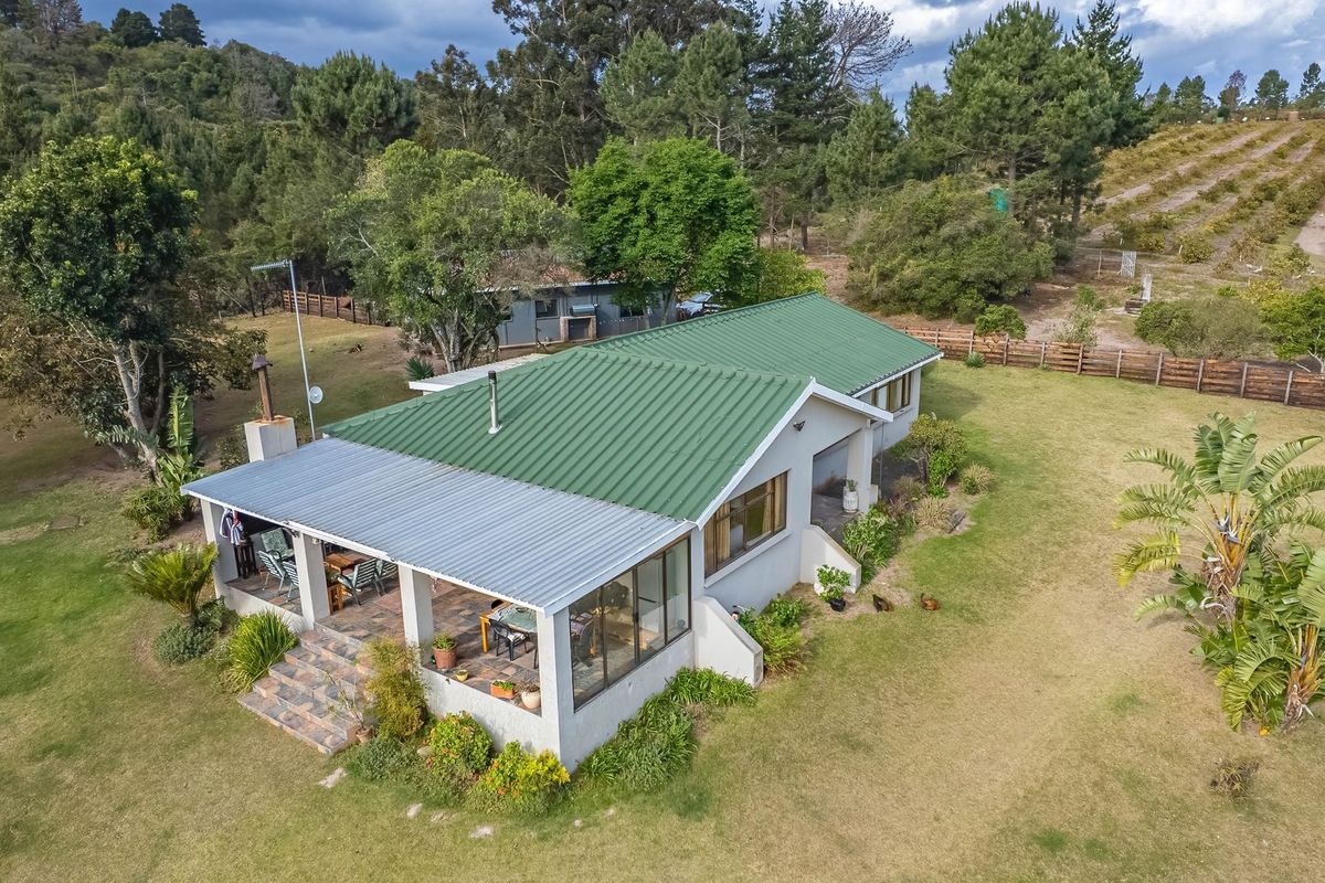 Aerial view of a farm property featuring a house with a green corrugated metal roof, a covered patio, and expansive surrounding grounds.