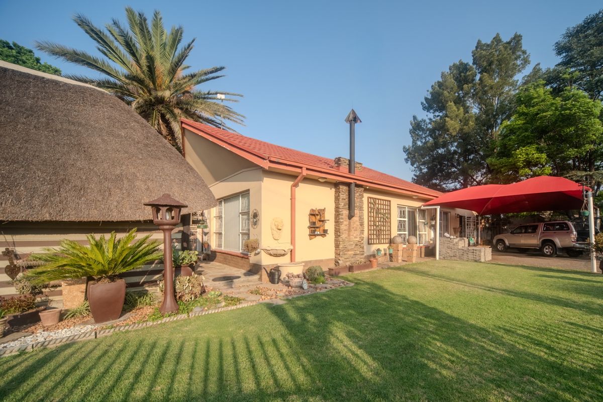 Rear view of the property featuring a combination of thatch and tiled roofing, a stone chimney, a paved patio area, and a well-maintained garden.