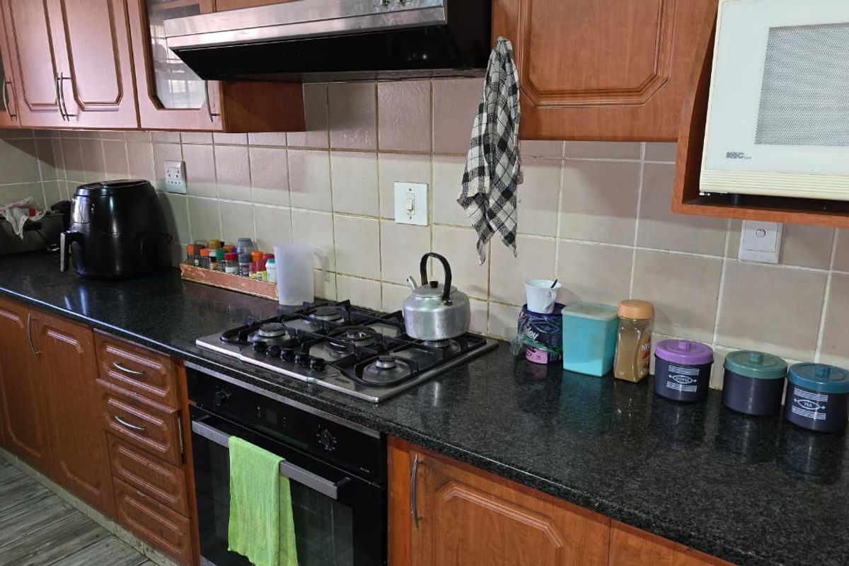 A functional kitchen featuring wooden cabinetry, granite countertops, a gas hob, built-in oven, and a tiled backsplash.