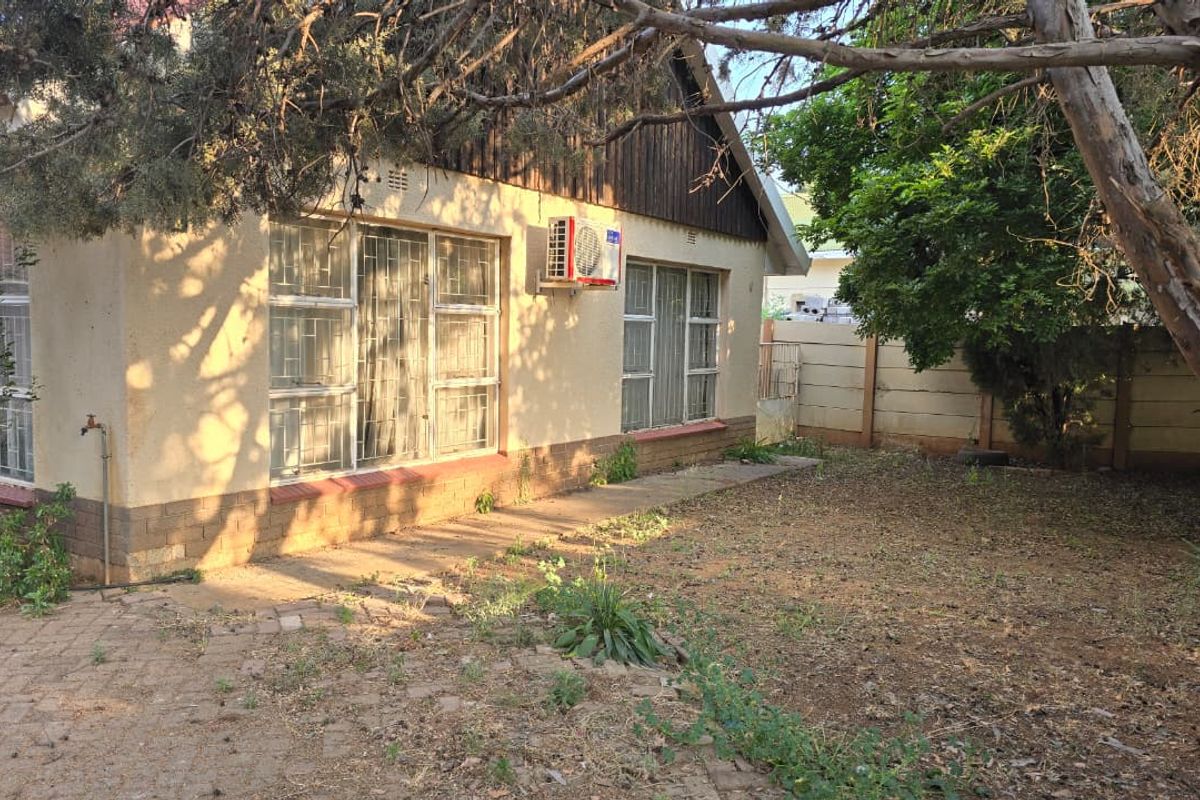 Rear exterior view of the house featuring a paved walkway, security bars on windows, and an installed air conditioning unit.