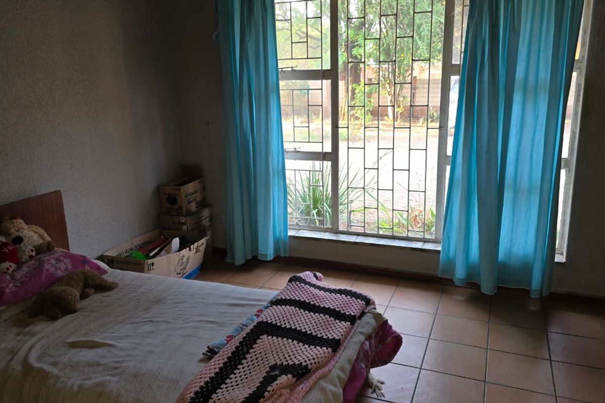 A bedroom featuring tiled flooring and a large window with security bars, requiring cosmetic updates to improve its overall appeal.