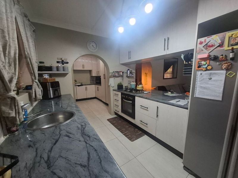 A functional kitchen featuring stone countertops, built-in cabinetry, a gas hob, and an integrated oven, connected to a secondary prep area via an archway.