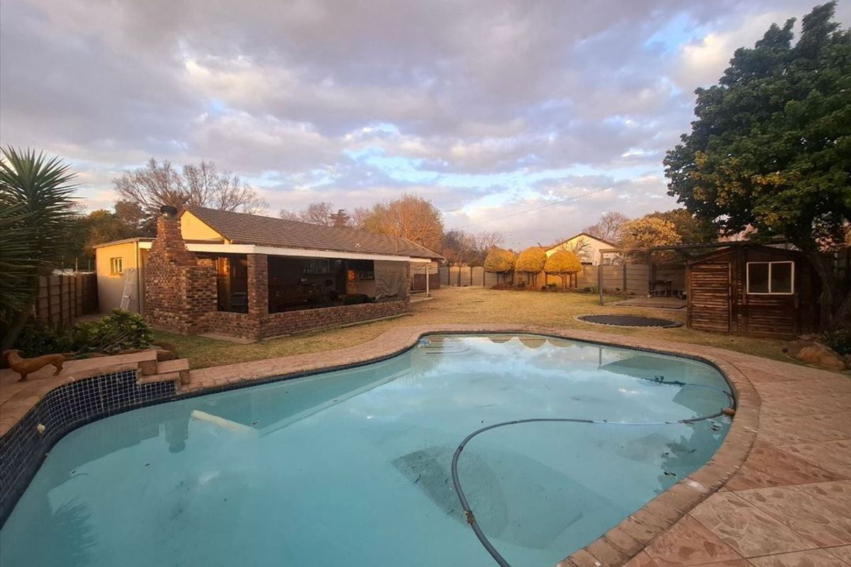 Spacious backyard featuring a swimming pool, covered patio area with brick chimney, and a timber storage shed set within a landscaped garden.