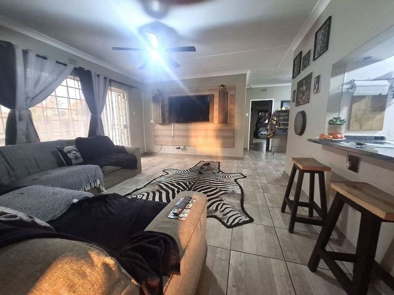 Open-plan living area featuring tiled flooring, a built-in media wall, and a breakfast bar connecting to the kitchen space.