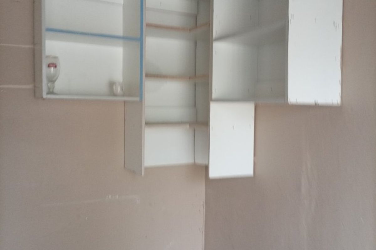 A corner section of a kitchen featuring incomplete wall-mounted cabinetry on unfinished walls, requiring renovation and finishing to become functional.