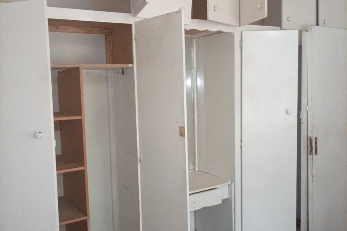 A bedroom featuring extensive built-in cabinetry with an integrated vanity and ornate ceiling detailing, requiring cosmetic updates and repairs to the cabinetry.