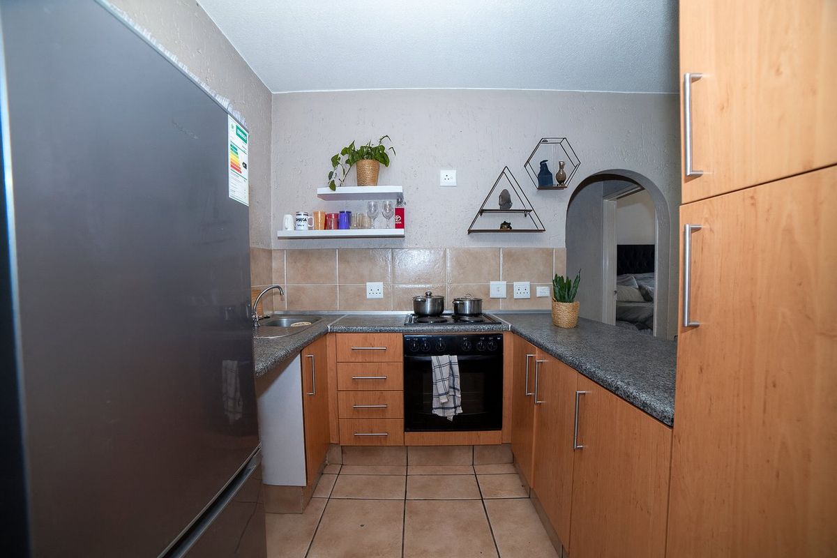 Compact kitchen featuring wood-finish cabinetry, granite-look countertops, tiled backsplash, and a built-in oven with hob.