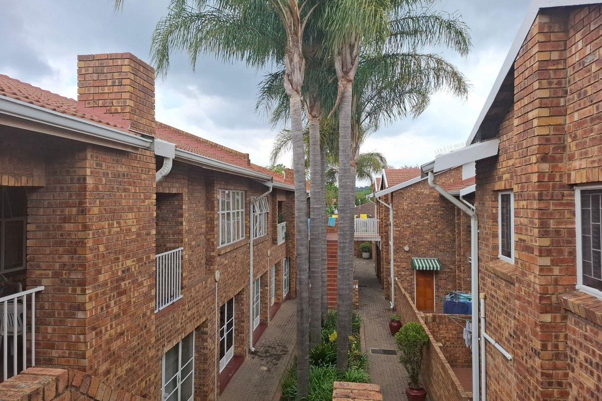 An elevated view of a townhouse complex courtyard featuring face brick architecture, paved walkways, and established palm trees between the residential units.