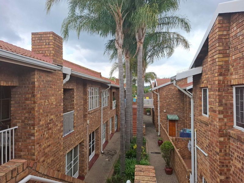 An elevated view of a townhouse complex courtyard featuring face brick architecture, paved walkways, and established palm trees between the residential units.