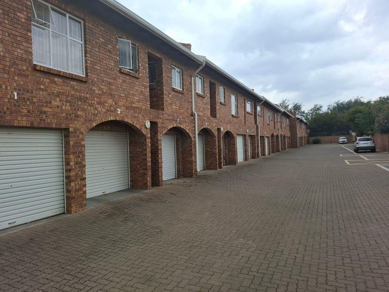 Exterior view of a townhouse complex featuring a row of brick garages with arched openings and a paved driveway.
