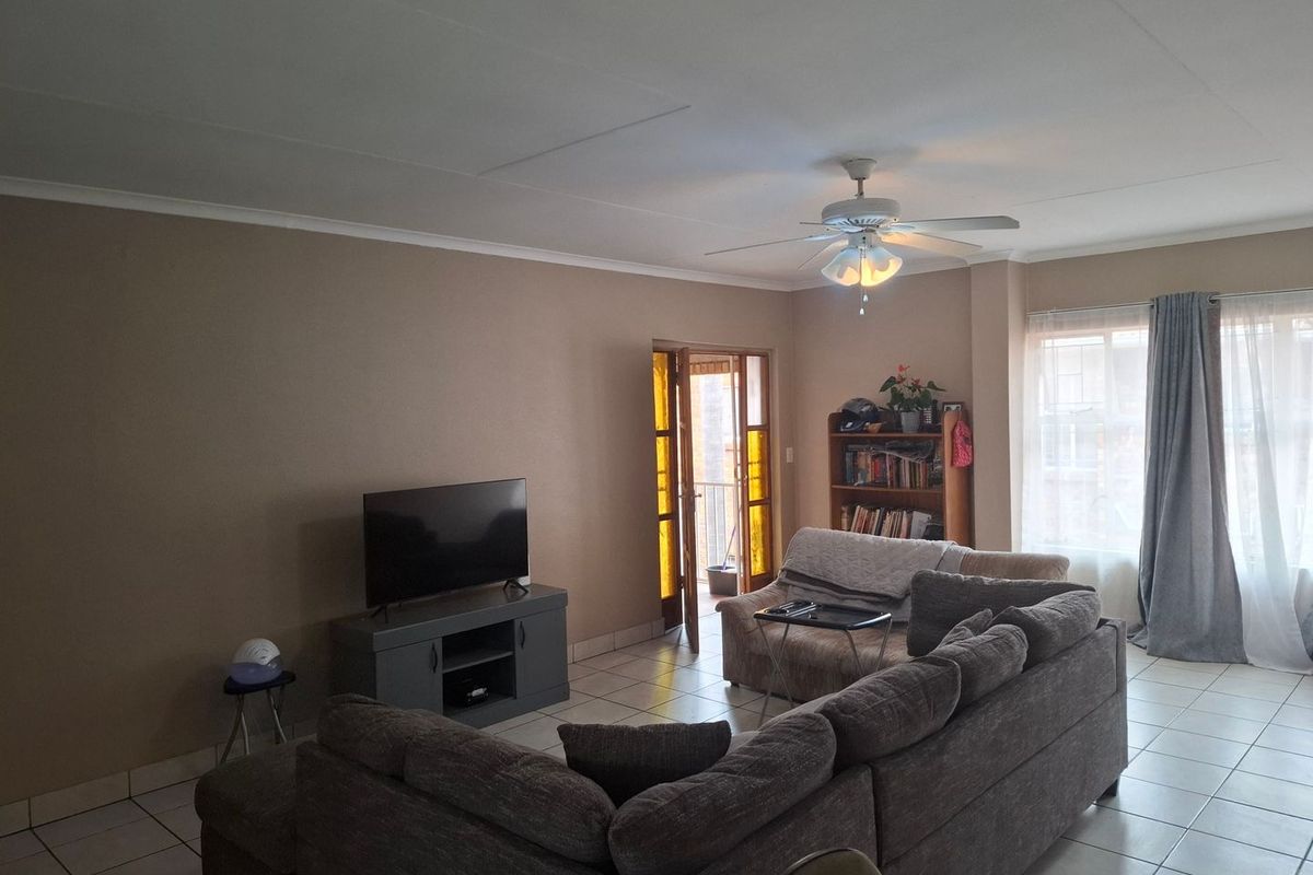 A spacious living room featuring tiled flooring, a ceiling fan, and direct access to an outdoor area through a glass panel door.