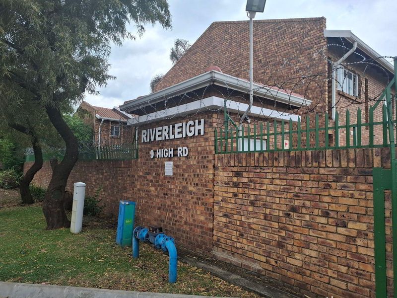 Front entrance view of Riverleigh complex showing face brick boundary wall, security fencing, and street-level utility infrastructure.
