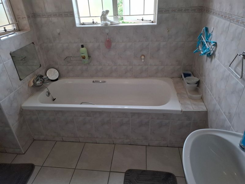 A functional bathroom featuring a built-in bathtub, tiled wall and floor finishes, and a window with security bars.