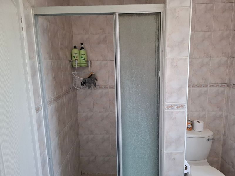 A functional bathroom featuring a shower enclosure with a sliding door and ceramic wall tiling throughout.