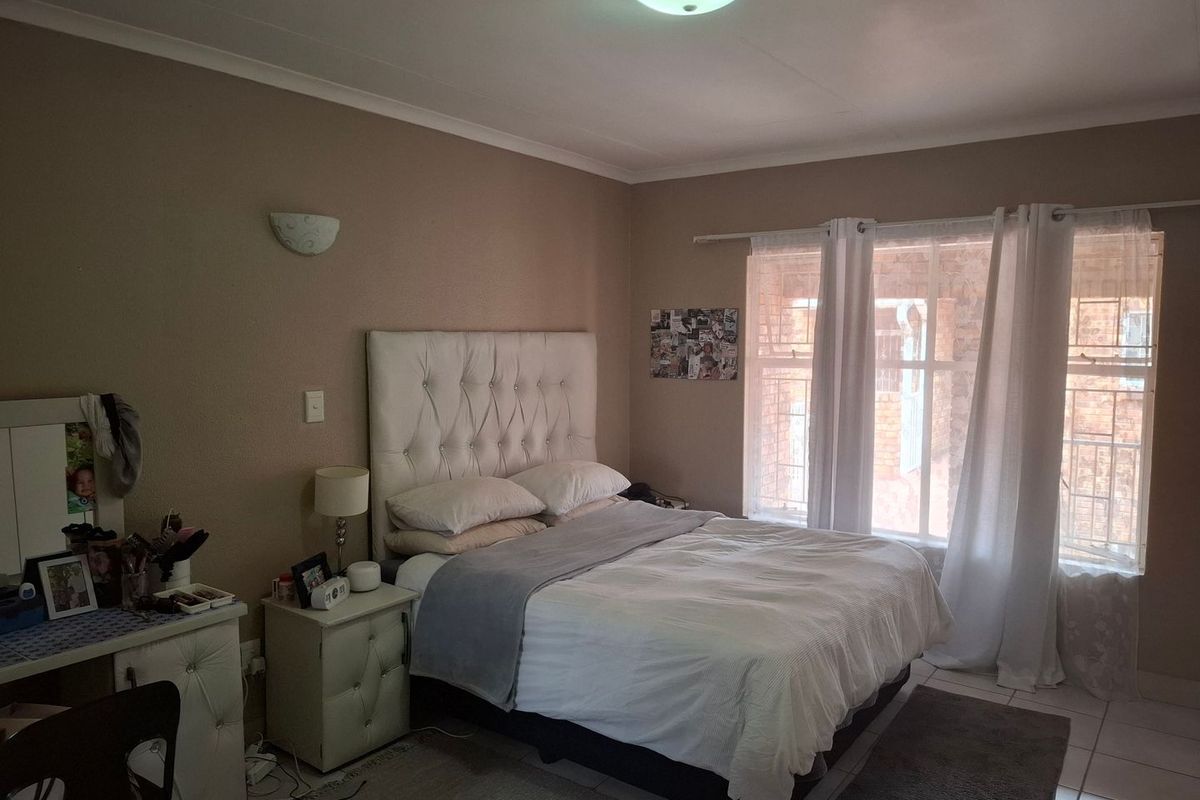 A bedroom featuring tiled flooring, a ceiling light, wall sconce, and a window fitted with security bars.