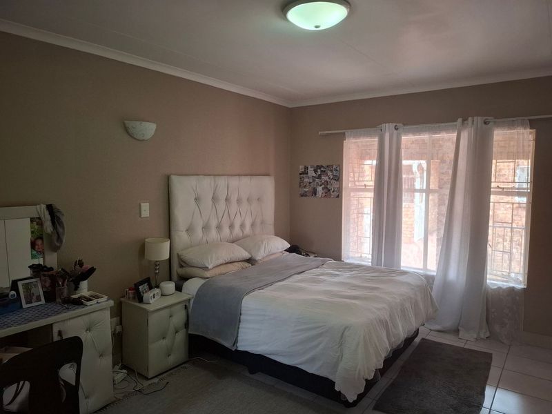 A bedroom featuring tiled flooring, a ceiling light, wall sconce, and a window fitted with security bars.