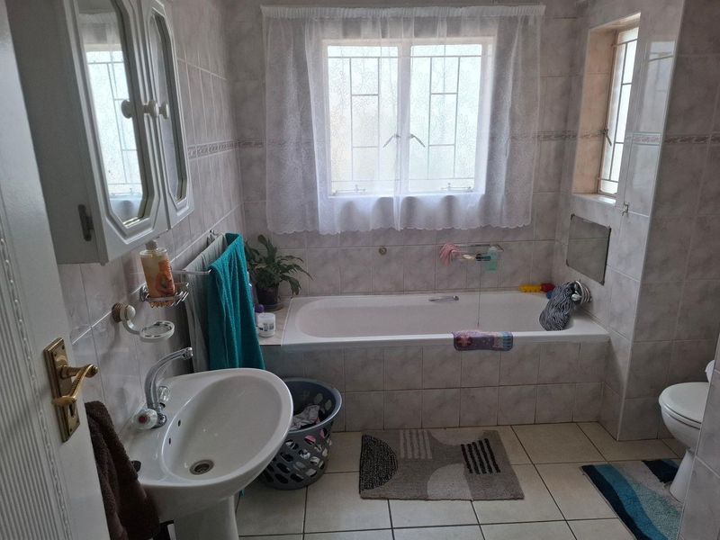 A functional bathroom featuring a pedestal washbasin, a built-in bathtub, and tiled finishes throughout, complete with security bars on the windows.