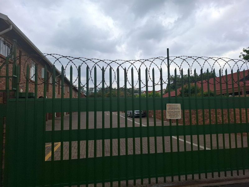 Secure gated entrance to a townhouse complex featuring brick paving and perimeter security fencing.