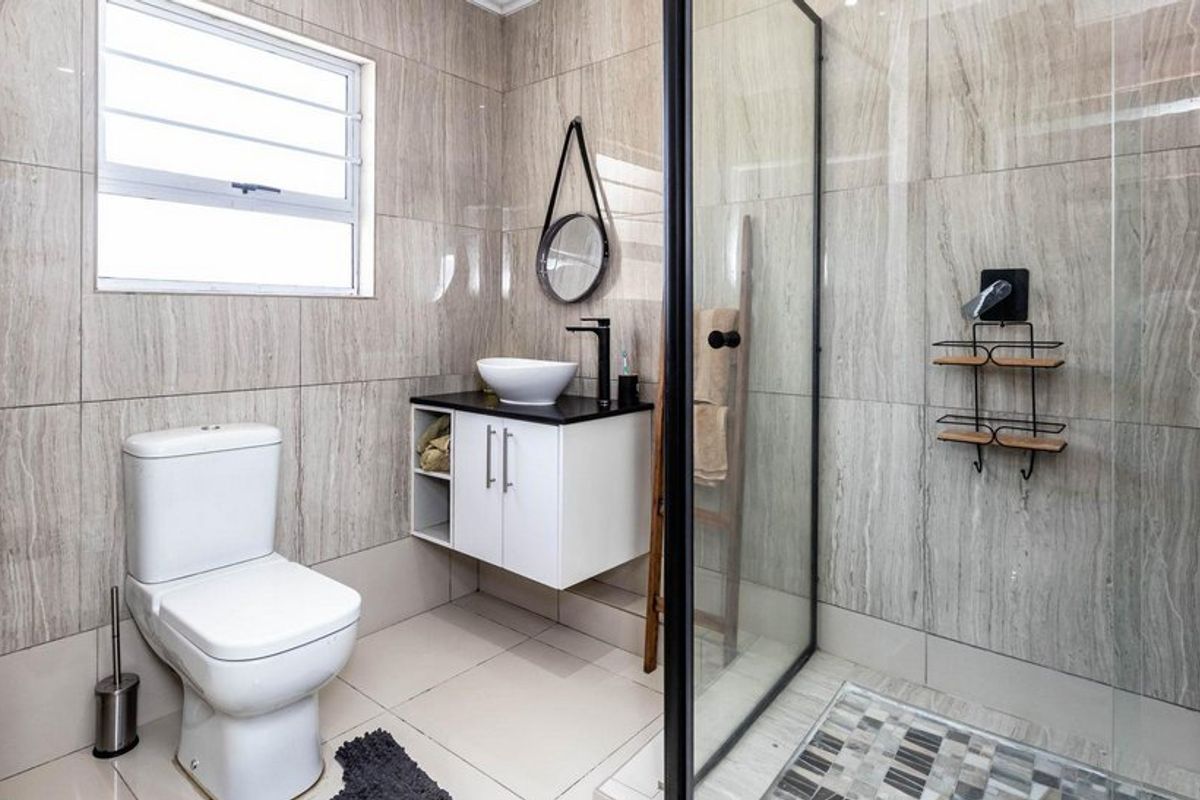 Modern bathroom featuring floor-to-ceiling tiled walls, a wall-mounted vanity with a vessel sink, and a spacious walk-in shower with a glass enclosure.