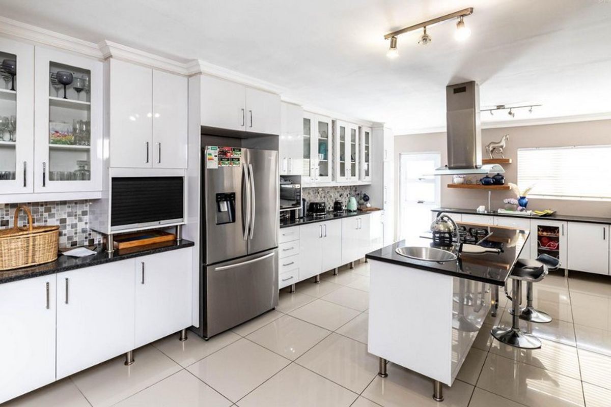 Modern kitchen featuring white cabinetry, granite countertops, a central island with a sink, stainless steel appliances, and a mosaic tile backsplash.