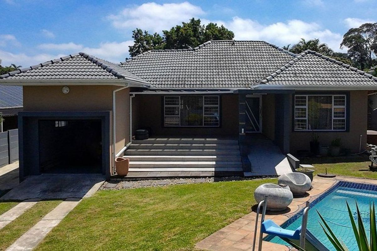 Rear view of the house featuring a tiled roof, covered patio, swimming pool, and attached garage set within a landscaped garden.