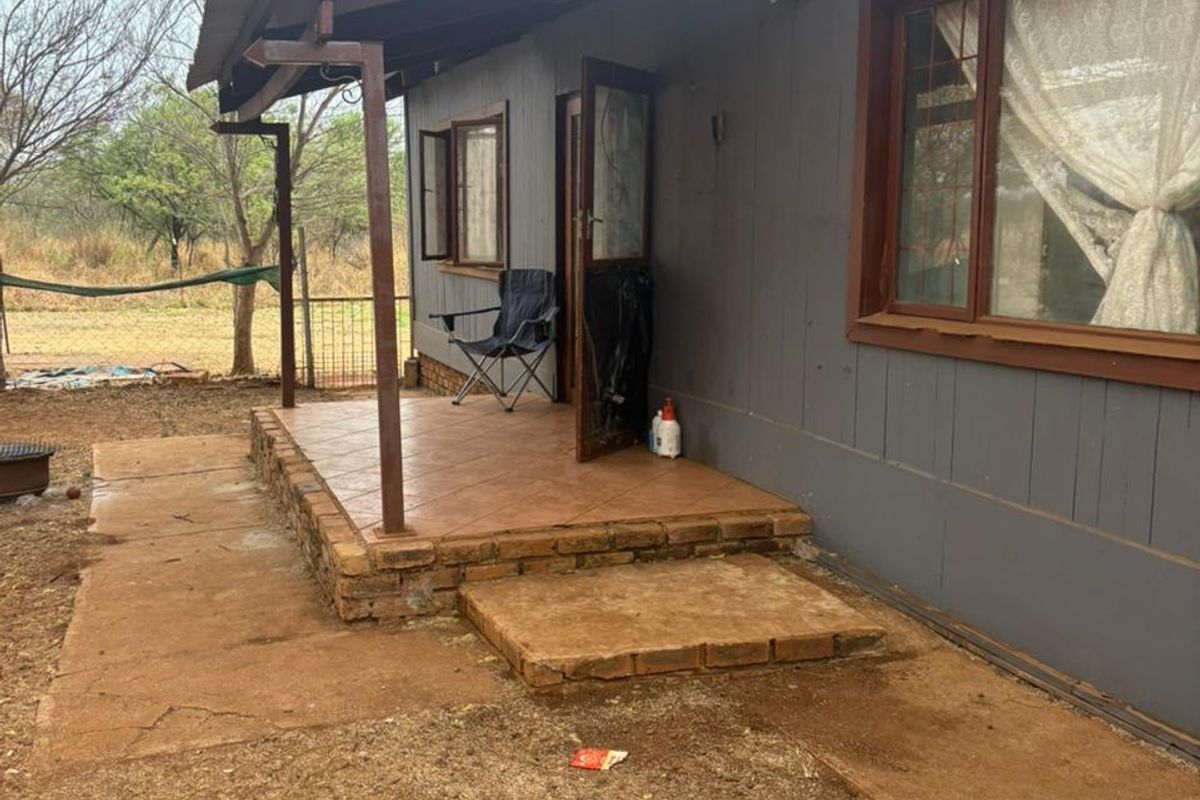Rear exterior view of the house featuring a tiled patio area, brick steps, and timber-framed windows with a corrugated metal roof.