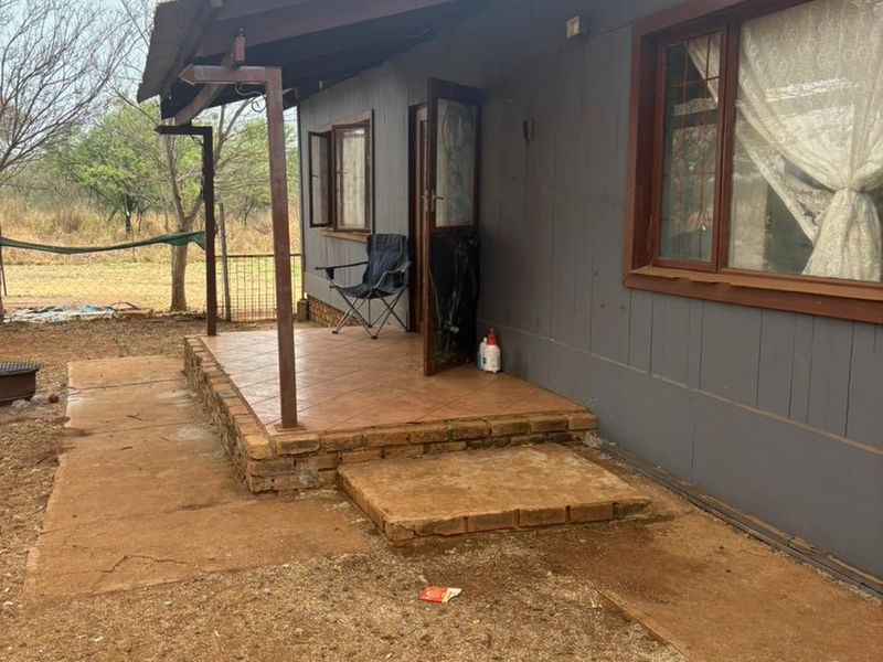Rear exterior view of the house featuring a tiled patio area, brick steps, and timber-framed windows with a corrugated metal roof.